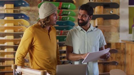 video of happy diverse male skateboarders fixing skateboard in skate shop
