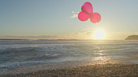 three vibrant red balloons play in wind as sun dips behind them in the sea