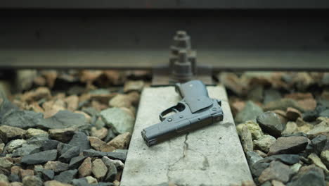 a close view of a handgun placed on the concrete base of a railway track surrounded by rocks