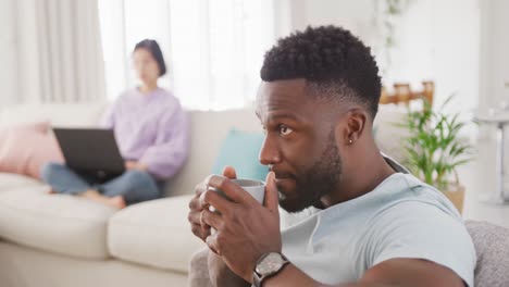 Pareja-Diversa-Tomando-Café-Y-Usando-Una-Computadora-Portátil-En-La-Sala-De-Estar