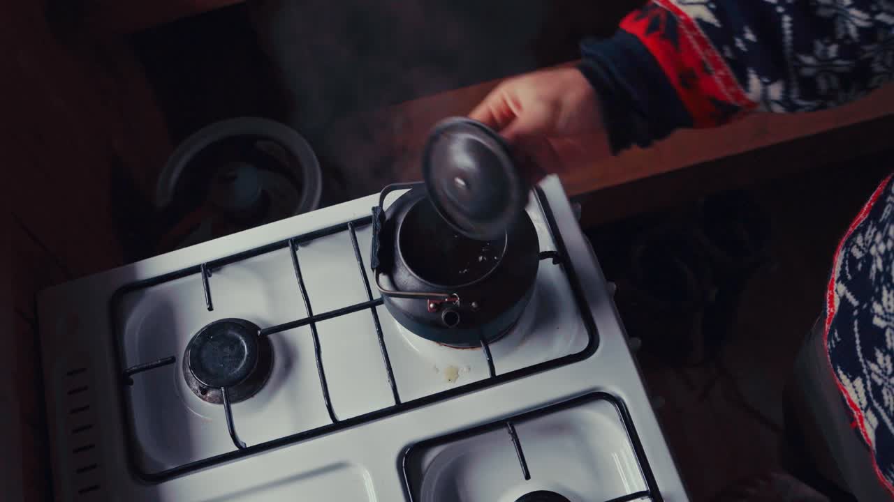 A Man Is Pouring Tea Powder Into A Boiling Kettle Over The Stove. High Angle Shot