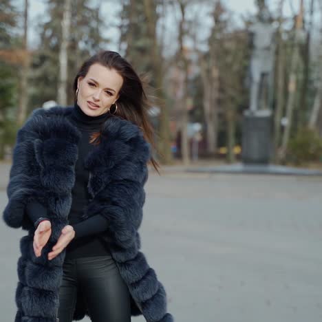 street portrait of a fashionable woman. young beautiful model wearing stylish black fur coat walking in the park. model posing on camera. street fashion concept.