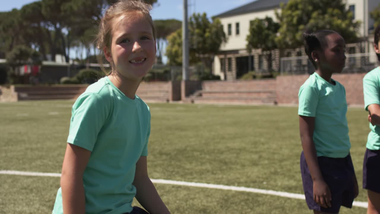 Crianças diversas do sexo feminino praticando, equilibrando o pé na bola de futebol, deslocando o peso na grama marcada