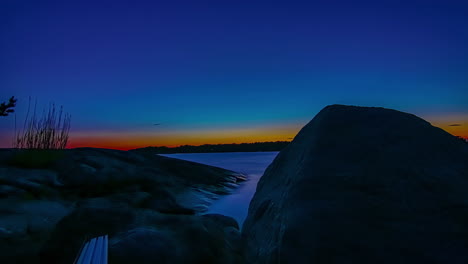 Hiperlapso-Hacia-Atrás-Al-Atardecer-Del-Agua-Moviéndose-En-La-Orilla-Rocosa-Del-Lago