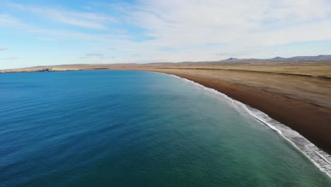 turquoise atlantic ocean waves crash on wide dark sand beach in santa cruz province, argentina.