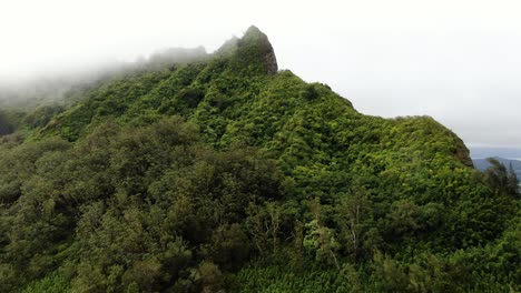 drone floating to the peak of a hawaiian mountain on oahu as rain clouds cover the island