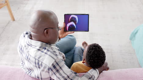 African-american-grandfather-and-grandson-using-tablet,-online-shopping-for-gamepads,-slow-motion