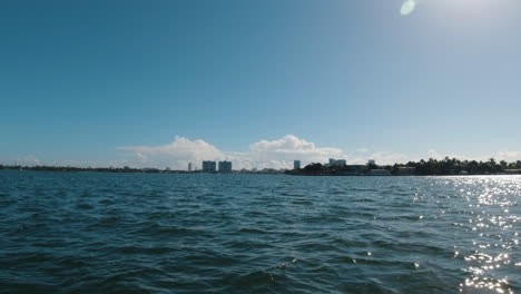 view from the bow of a small watercraft as it speeds toward the city on the horizon miami florida as the sun reflects off the water of the bay