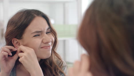 Upset-woman-taking-off-earrings-from-ear-looking-in-bathroom-mirror