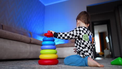 toddler kid sits in the room busy with a game. baby boy building a colorful pyramid. low angle view.