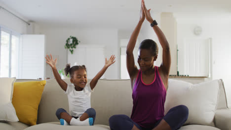 Feliz-Madre-E-Hija-Afroamericana-Sentadas-En-Un-Sofá-Haciendo-Ejercicio-De-Yoga-En-Casa