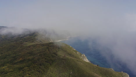 bird's eye view of a breathtaking steep rocky coast line with heavy dense fog approaching from the sea, far east, russia, sea of japan