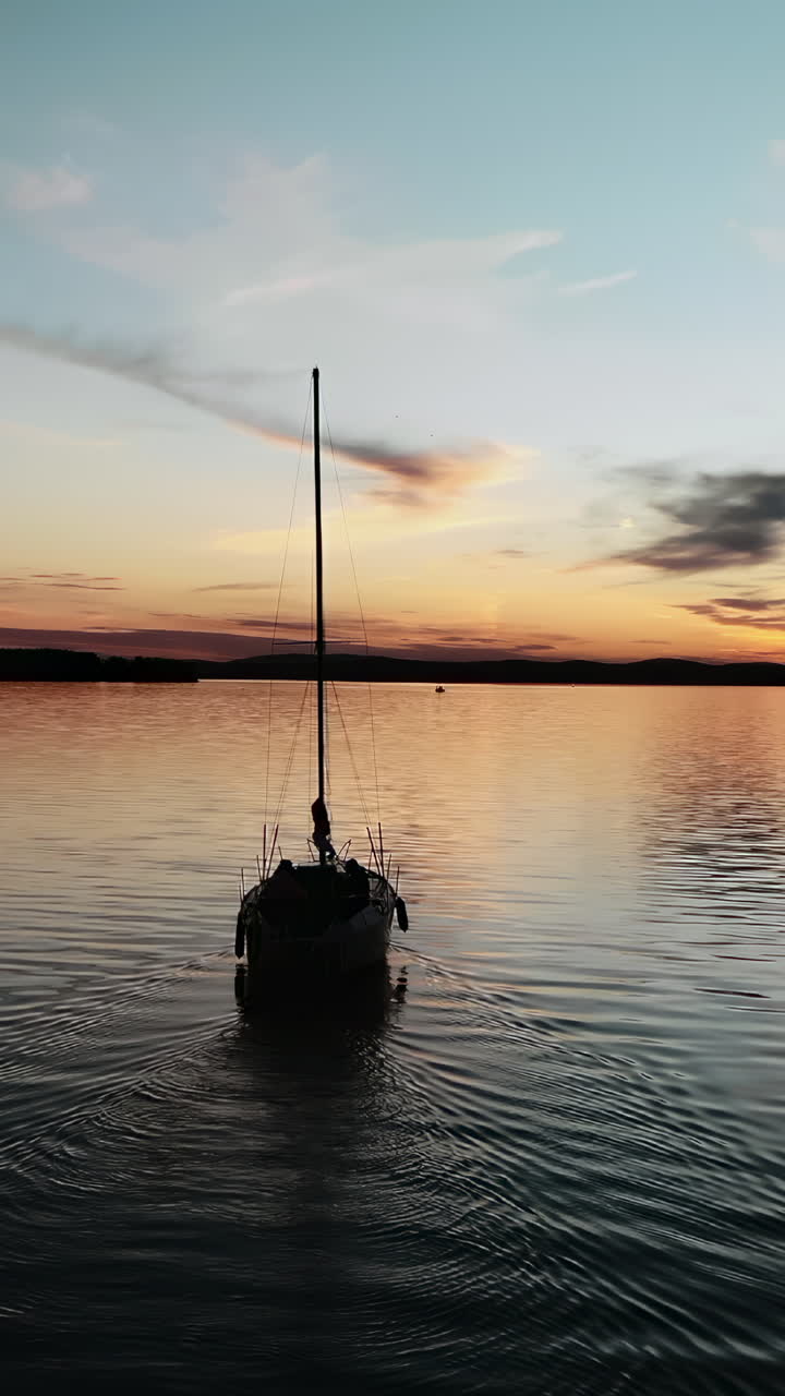 Barca a vela in silhouette che galleggia su acque calme con un bellissimo tramonto che si riflette sulla superficie