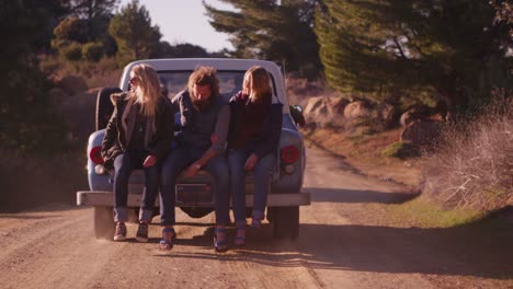 Eine-Gruppe-Von-Freunden-Sitzt-Auf-Der-Ladefläche-Eines-Pickups,-Der-Eine-Landstraße-Entlang-Fährt-1