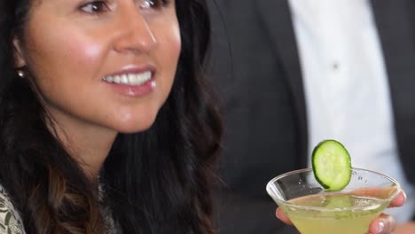 una joven asiática sostiene un lujoso martini de pepino en un cóctel mientras escucha y está de acuerdo con alguien que habla en un grupo de personas