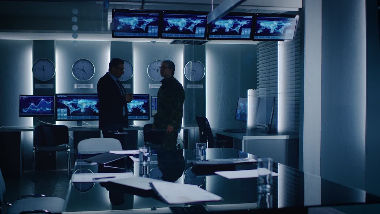 연방 특수 요원이 감시실에서 군인과 대화합니다. 배경에는 데이터 흐름을 보여주는 모니터와 함께 바쁜 시스템 제어 센터가 있습니다.
