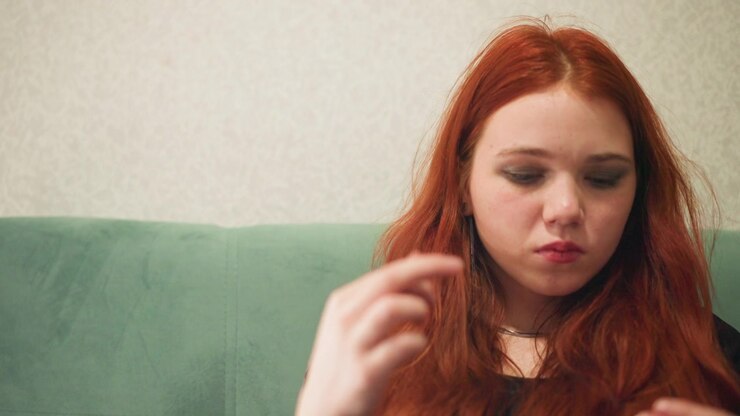 Young caucasian woman inspecting ring on green sofa, slow methodical movements and subtle lip bite, pondering significance of heirloom and future choices, intimate livingroom portrait with soft