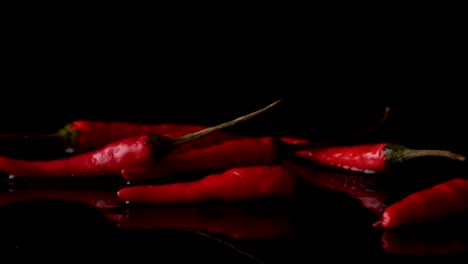 falling red peppers on wet surface against black background