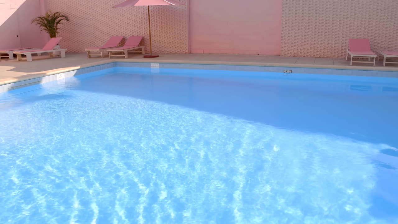 Tom swimmingpool med lyserøde liggestole og parasol på en solrig dag