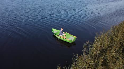 über-Dem-Wasser:-Drohnenansicht-Eines-Flusses,-Eines-Fischerbootes-Und-Eines-Anglers-Im-Schilf