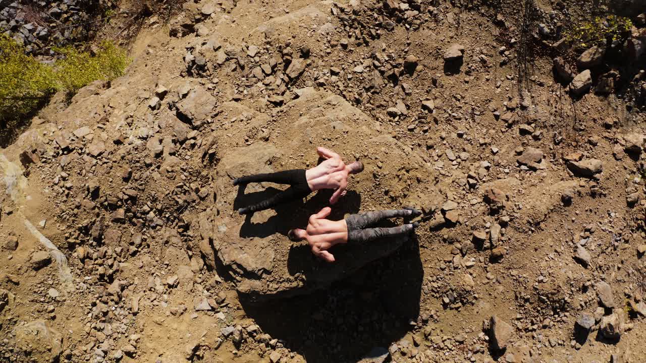 Top view on two sportsmen doing push-ups on rocks. Shirtless young athletes doing push ups on the hill in summer day. Aerial view.