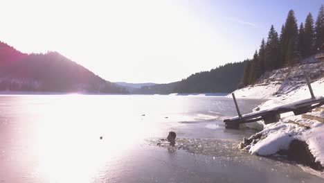 Sunlight-shines-and-reflects-on-frozen-surface-of-remote-mountain-lake-with-cabin-in-background