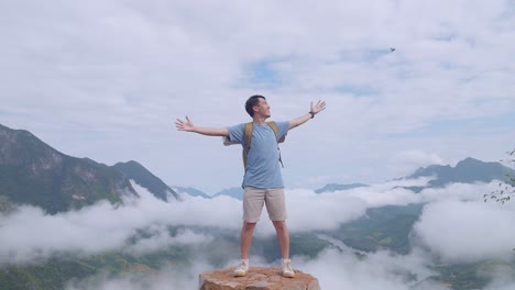 asian hiker male standing on the rock and raising his hands celebrating reaching up top of foggy mountain