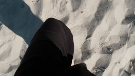 bare feet of woman in black pants walking on sand