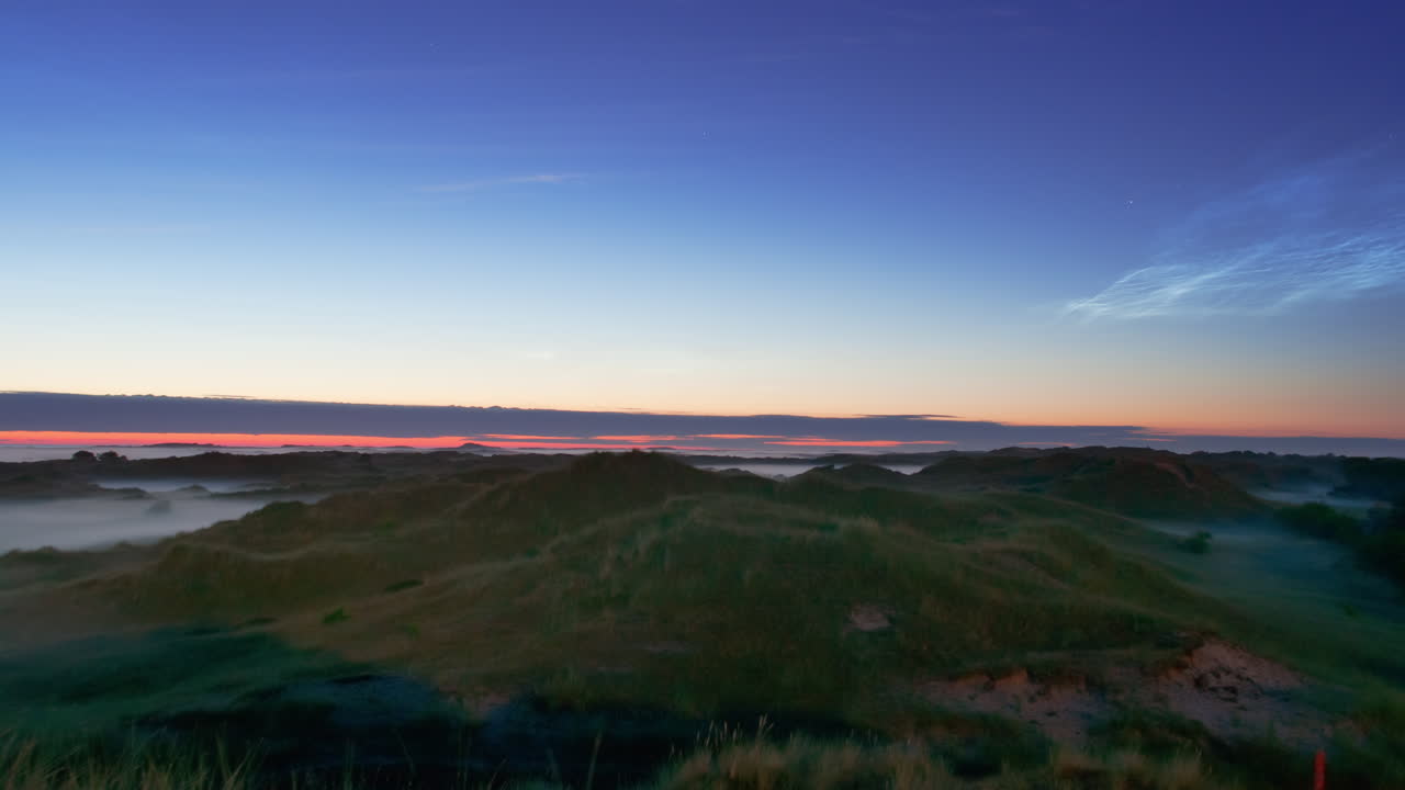 noctilucent clouds NLC with early morning fog over landscape island North Sea in summer twilight timelapse