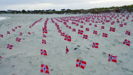 aerial view flying over multiple norway flags on sandy beach coastline blowing in wind