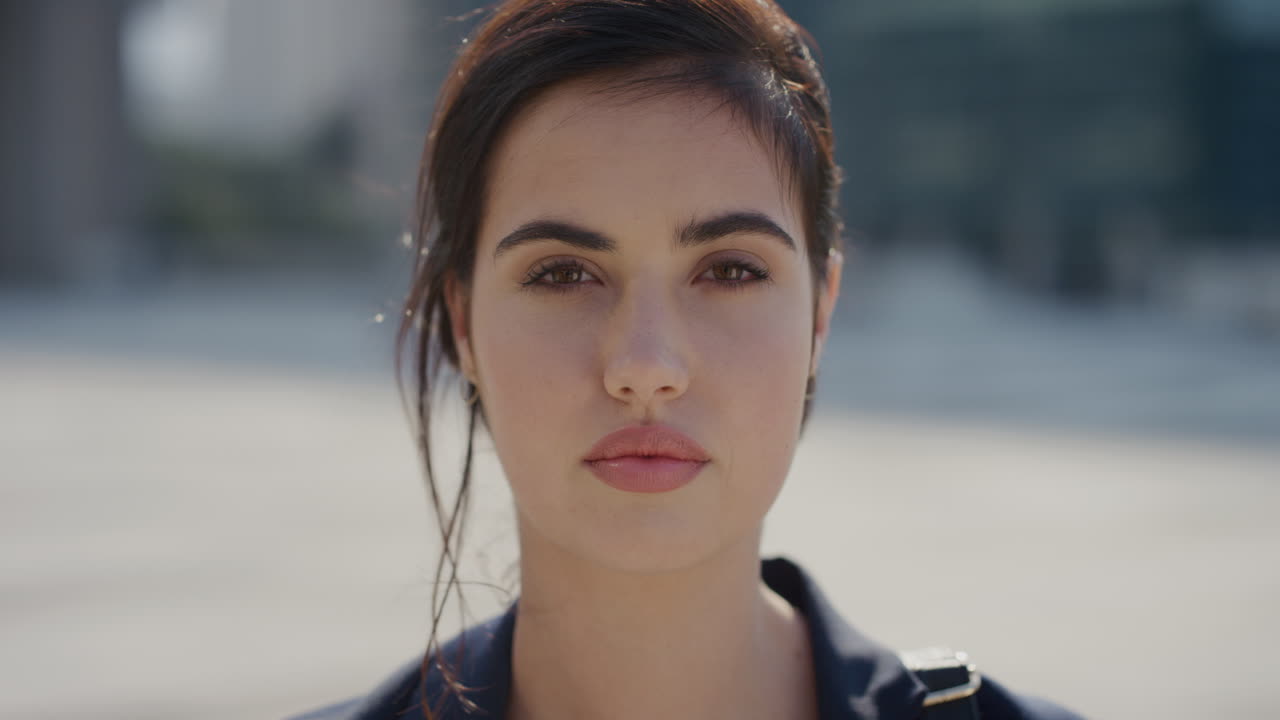 retrato de una hermosa mujer joven que gira la cabeza buscando una mujer de negocios independiente y seria en una ciudad urbana soleada donde el viento sopla en cámara lenta