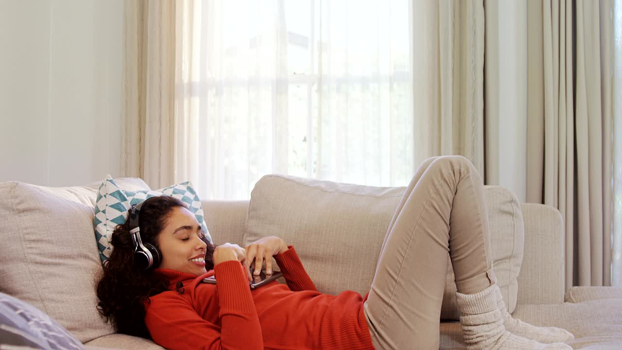 4k 4k 헤드폰에서 음악을 즐기는 태블릿을 사용하여 소파에 누워있는 행복한 여성