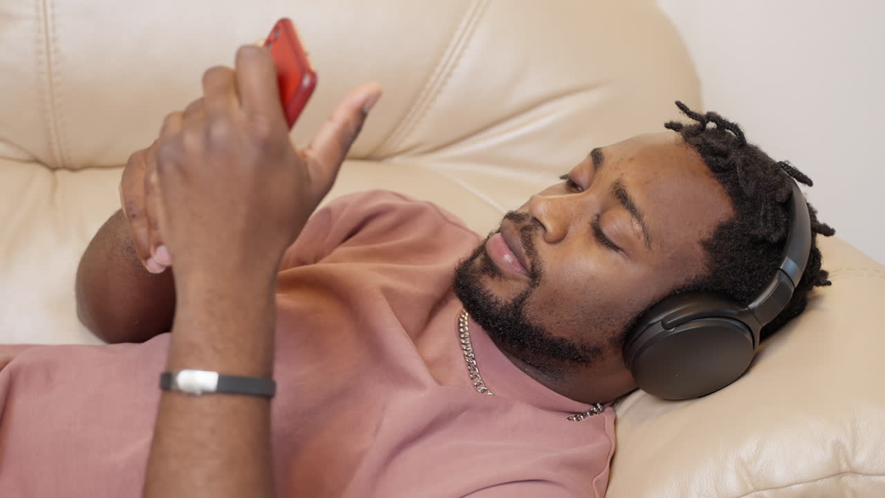 hombre relajándose en el sofá usando teléfono inteligente y auriculares