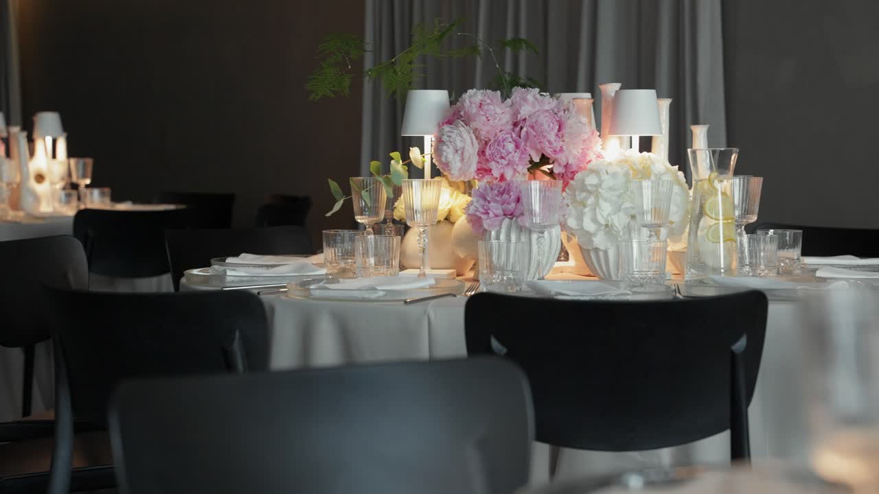 Stylish wedding reception setup with elegant floral centerpieces, soft candlelight, and modern table arrangements in a dimly lit, romantic indoor venue