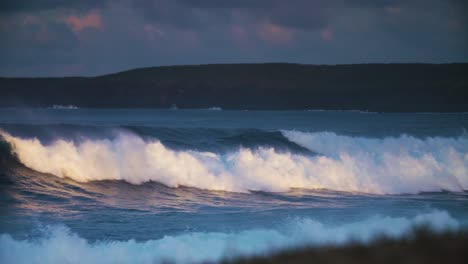 waves crash against a rocky shore in golden light