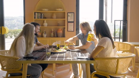 vista lateral de un grupo de amigos hablando sentados en la mesa del restaurante mientras uno de ellos corta una pizza