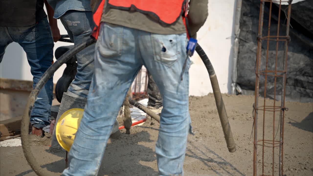 Slow motion of fresh concrete mix being pumped onto grid at a construction site in Mexico to create the house slab while workers use a concrete vibration machine