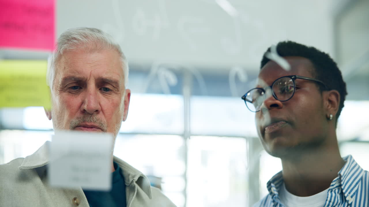 Two Diverse Businessmen Collaborating and Brainstorming on a Glass Board in an Office