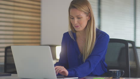 Joven-Empresaria-Trabajando-Hasta-Tarde-Sentada-En-Un-Escritorio-Con-Una-Computadora-Portátil-En-Una-Oficina-Moderna-Y-Abierta