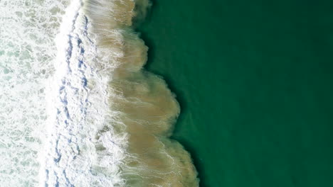 Downward-drone-shot-of-waves-crashing-on-sand-at-Cabarita-Beach