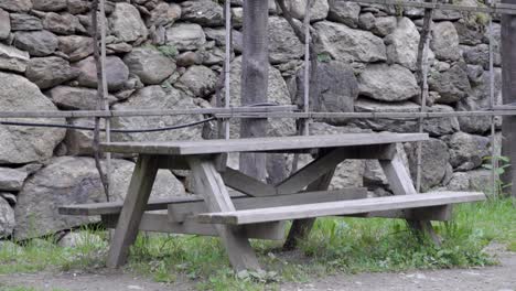 wooden outdoor picnic table with two integrated benches in front of a stone wall