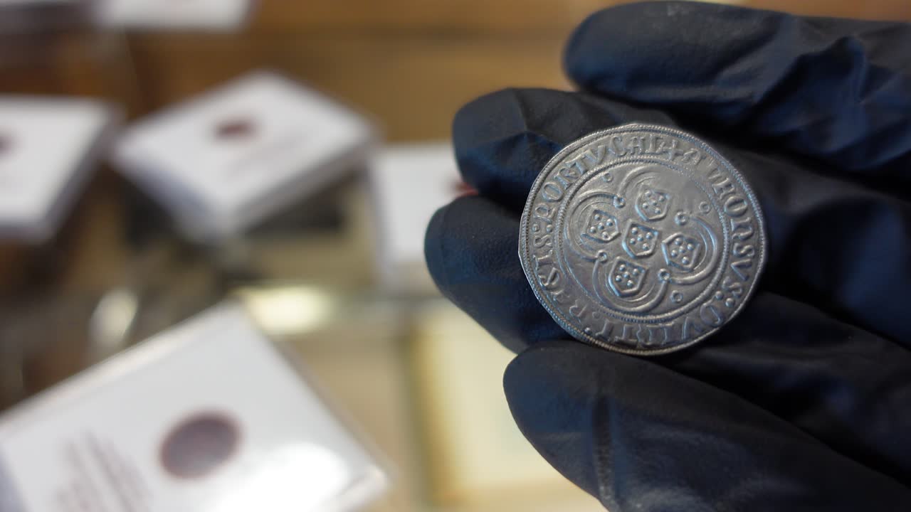 coleccionista examinando una moneda de oro portuguesa de la época medieval