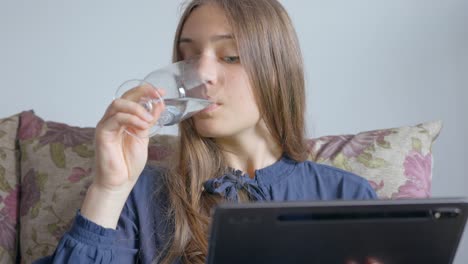 Stable-shot,-girl-drinking-water-from-tall-glass-while-reading-book-on-tablet