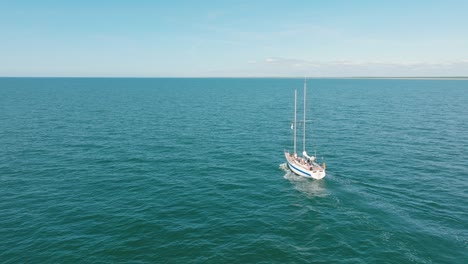 aerial establishing view of a white sailboat in the calm batltic sea, white sailing yacht in the middle of the boundless sea, sunny summer day, wide ascending done shot moving forward