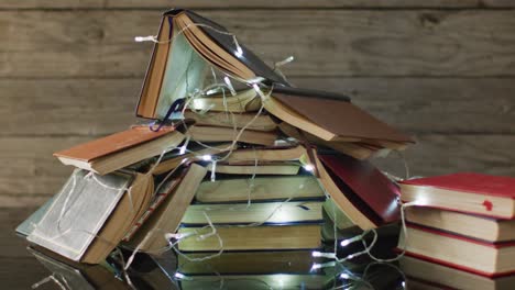 video of christmas fairy lights and stack of books on wooden background