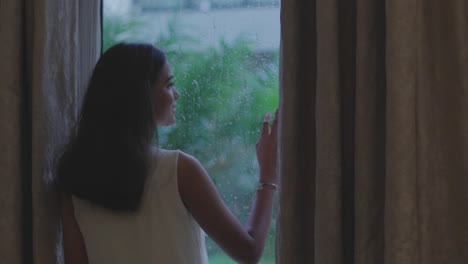 Close-up-shot-of-woman-removing-curtain-to-see-rain-from-window-in-Diu-city-of-India