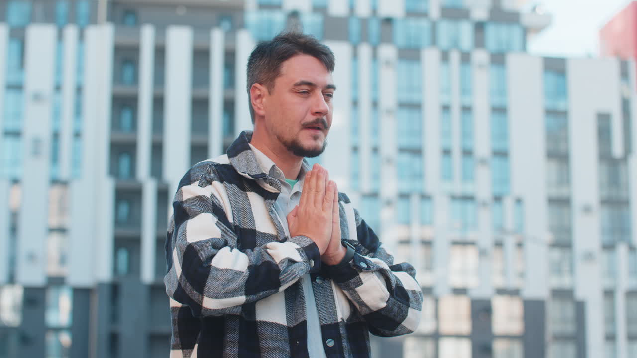 Mature caucasian man tourist standing on city street folding palms praying asking god for help