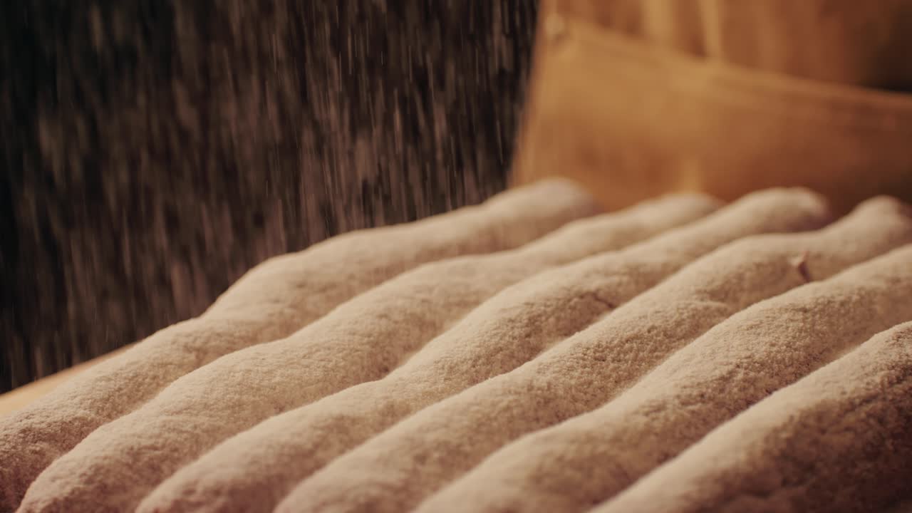 Bakery chef applying flour on dough, young man kneading dough, making bread using traditional recipe. Artisan bread is making by skill bakers using natural and high-quality ingredients. Food with health and flavour benefits.