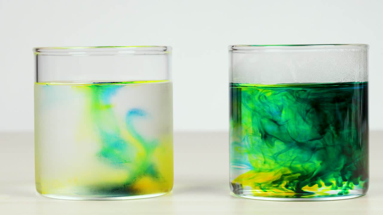 Food coloring disperses in two glasses of hot and cold water under bright, even lighting