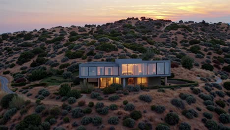warm lights glowing within a modern architectural marvel on a hillside, as the sun setting paints the sky in orange and purple, creates a serene, luxurious atmosphere